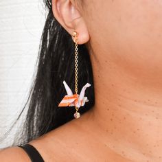 a close up of a person wearing earrings with origami birds hanging from them