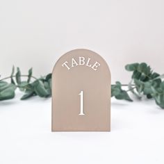 a table number is placed on top of a wooden plaque with white lettering and green leaves