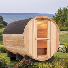 a wooden sauna in the middle of a grassy area next to trees and water