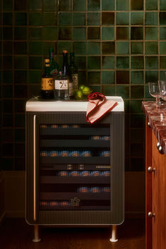 a wine cooler sitting on top of a wooden counter next to some bottles and glasses