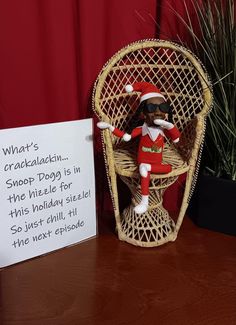 an elf doll sitting in a wicker chair next to a sign that says, what's crazilladii shop dog is in the hole for this holiday season