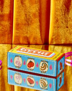 two boxes with different types of food on them sitting in front of a yellow curtain