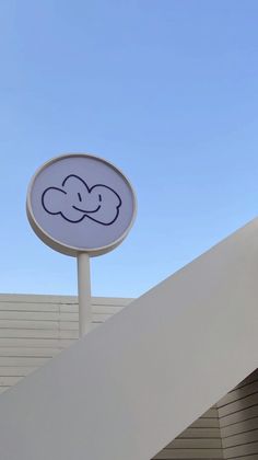 a sign with a smiley face drawn on it next to a white building and blue sky