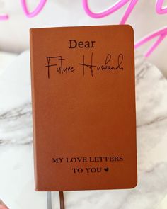 a book with writing on it sitting on top of a white marble table next to a pink neon sign