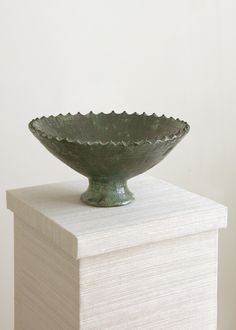 a green bowl sitting on top of a stack of books in front of a white wall