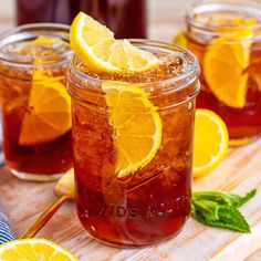 three mason jars filled with iced tea and lemon slices on a cutting board next to two spoons