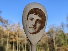 a wooden spoon with an image of a young man on it's side and trees in the background