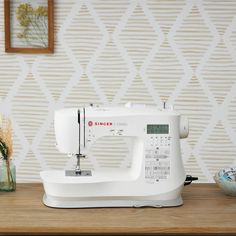 a white sewing machine sitting on top of a wooden table next to a vase with flowers