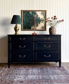 a black dresser with two vases on top of it and a painting hanging above