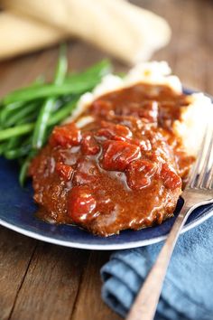 a blue plate topped with meat covered in gravy and green beans