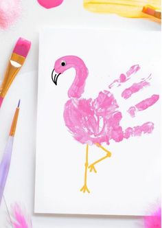 a pink flamingo handprint on a white paper with paintbrushes next to it