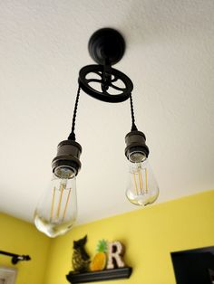 two light bulbs hanging from the ceiling in a room with yellow walls and pictures on the wall