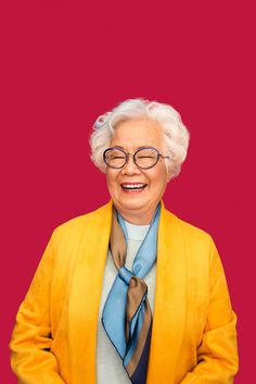 an old woman wearing glasses and a yellow jacket with a blue neck tie smiling at the camera