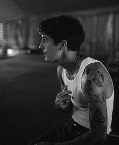 black and white photograph of a man with tattoos on his arm sitting in an empty parking lot