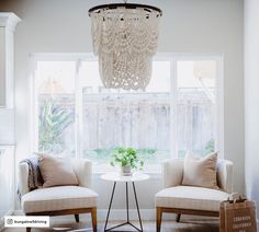 a living room with two chairs and a chandelier hanging from the ceiling in front of a window