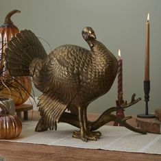 a bronze turkey figurine sitting on top of a table next to candles and pumpkins