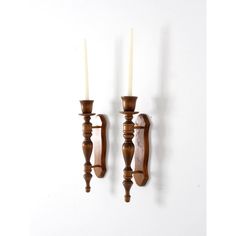 two wooden candlesticks on a white wall with one candle in between them and the other