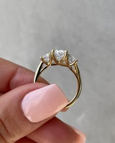 a woman's hand holding a gold ring with three diamonds on it and a pink manicured nail