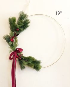 a christmas wreath with pine branches and red ribbon hanging on a white wall next to a measuring tape