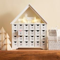 a white wooden house shaped calendar sitting on top of a table next to a small christmas tree