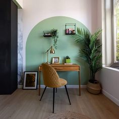 a room with a desk, potted plant and pictures on the wall next to it