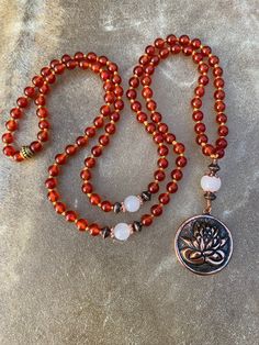 Distinct & beautiful, 108 red orange Carnelian beads with white Jade accents and a 100% copper Lotus Flower amulet. The Lotus flower is an auspicious symbol in many cultures. It grows from the depth of murky, muddy waters and represents rising above darkness and illusion.  In Buddhism & Hinduism the beautiful flower has come to be associated with purity, beauty, spiritual awakening & faithfulness.  Carnelian promotes courage, high energy, motivation & protection. White Jade is said to promote he Red Agate Beaded Bracelet For Meditation, Red Agate Beaded Bracelets For Meditation, Red Carnelian Beaded Bracelets With Gemstone Beads, Red Beaded Bracelets With Natural Stones For Meditation, Red 8mm Beads Healing Jewelry, Red 8mm Beads Jewelry For Meditation, Red 8mm Beads Jewelry For Healing, Red Hand-strung Jewelry For Meditation, Red Carnelian Beaded Bracelet With Round Beads