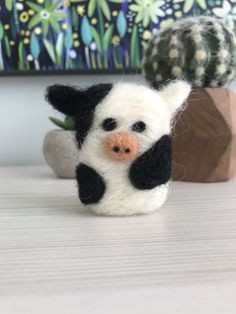 a small black and white cow sitting on top of a table next to a cactus