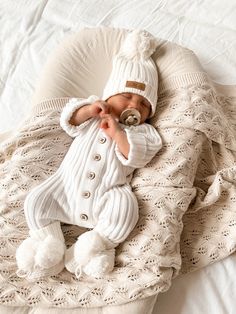 a baby wrapped in a blanket on top of a white bed next to a pillow