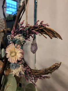 a dried flower wreath hanging from a branch with purple and white flowers in the center