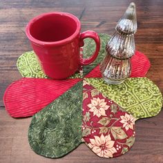 a red mug sits on top of four coasters with green and red designs, along with a silver coffee cup