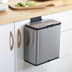 a stainless steel trash can mounted to the side of a kitchen counter next to a cutting board