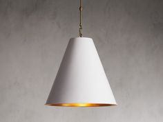 a white lamp hanging from a gold colored chain on a gray wall with concrete flooring