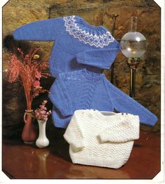 a blue sweater and white bag sitting on top of a table next to a vase with flowers