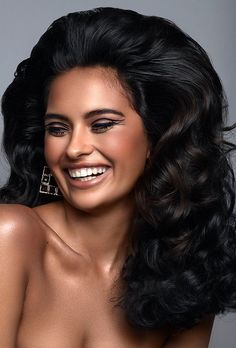 a smiling woman with long black hair and large earrings on her head is posing for the camera