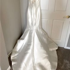 a white wedding dress hanging on the wall in front of a door and carpeted floor