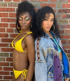 two women standing next to each other in front of a brick wall