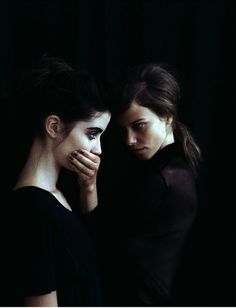 two women standing next to each other in front of a black background with their hands on their face