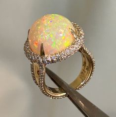 One-of-a-kind 16mm Genuine Ethiopian Confetti Opal Cabochon set in 18ky Gold with a Diamond Halo made of 2-point diamonds, and 2-point diamonds going down each side of the shank. Size 6.25 Luxury Halo Opal Ring For Formal Occasions, Luxury Ethiopian Opal Ring, Luxury One-of-a-kind Ethiopian Opal Jewelry, Luxury Ethiopian Opal Ring For Anniversary, Luxury Handmade Ethiopian Opal Ring, Luxury Yellow Gold Opal Ring, Luxury Yellow Gold Cabochon Diamond Ring, Luxury Round Cabochon Diamond Ring, Luxury Gold Opal Ring With Diamonds