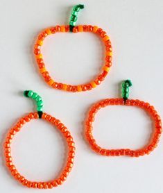 three orange and green beaded bracelets on a white surface with two small beads attached to them