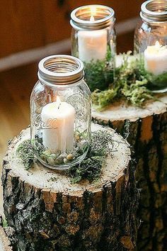 three mason jars filled with candles sitting on top of a tree stump