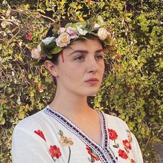 a woman with flowers in her hair wearing a white shirt and floral head wreath on her head