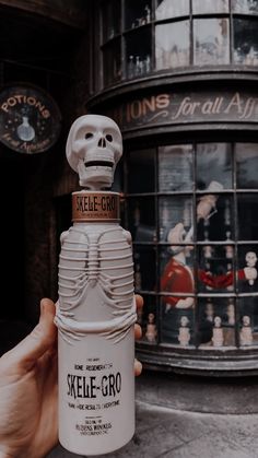 a person holding up a skeleton bottle in front of a building with an advertisement for skele - gro on it