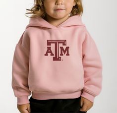 Aggie Pride, Toddler Style: Our Toddler Texas A&M Logo Hooded Sweatshirt is the perfect blend of comfort and collegiate spirit for the smallest Aggies. This charming hoodie showcases the beloved Texas A&M logo, making it an ideal choice for game day festivities or everyday wear. Crafted with a soft, jersey-lined hood and made from durable, child-friendly materials, it provides essential warmth and ease of movement for active toddlers. The robust construction ensures it can stand up to the rigors Collegiate Hooded Tops For College, Collegiate Sweatshirt With Adjustable Hood, Collegiate Hoodie For Fall Fan Gear, Varsity Hoodie For Fall Fan Gear, School Varsity Hooded Sweatshirt, Varsity Hoodie With Team Name For Fall, School Spirit Hoodie For Fall, School Spirit Hooded Hoodie For Fall, Fall Varsity Hoodie For School