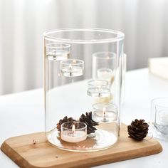 a candle holder with pine cones and candles in it on a wooden tray next to two glasses