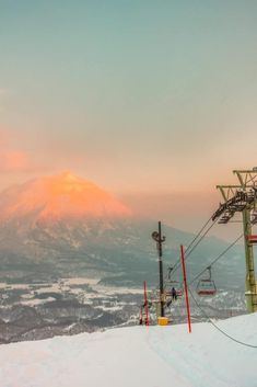 a ski lift going up the side of a snow covered slope at sunset with mountains in the background