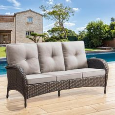 a couch sitting on top of a wooden floor next to a swimming pool with a house in the background