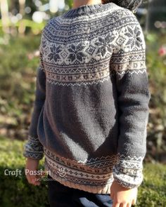 a little boy wearing a hat and sweater in the grass with his hands on his hips