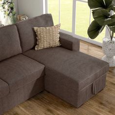 a brown sectional couch sitting on top of a hard wood floor next to a window