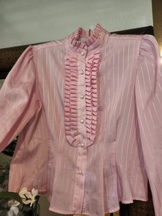 "This adorable silky pink blouse by Doo Dads has a silky comfortable feel. Rockin' the tuxedo style front ruffles with 6 pearl buttons down the front.  It has a high Victorian collar with tux ruffle as well. The fabric has a classy shiny striped pattern. The long sleeves have 1 pearl button at the cuff. There are 4 darts on the front bodice to accentuate your curves. This blouse is in great vintage shape. There is only a small faint blemish on back below the waist (see Pics) Will most likely wash out. Hard to see. Measurements- Chest: 40\" Waist\" 34\" Length: 22\"" Red Velvet Gown, 60s Fashion Dresses, Victorian Collar, Tuxedo Style, White Polka Dot Dress, Velvet Gown, Gown Photos, Pink Ruffle, Pink Blouse