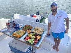 a man standing next to a table full of food on a boat in the water